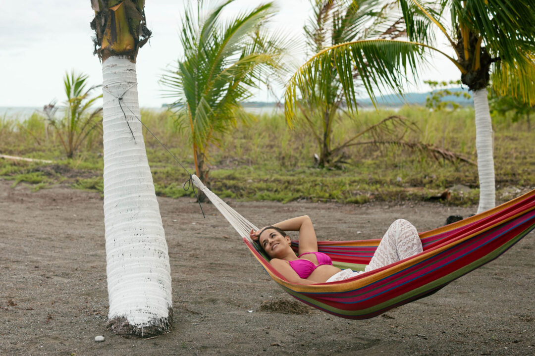 Woman relaxing in hammock beneath trees on brach.